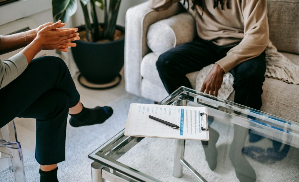 Crop anonymous African American man in casual clothes sitting on sofa and talking to female psychologist during psychotherapy session in modern studio